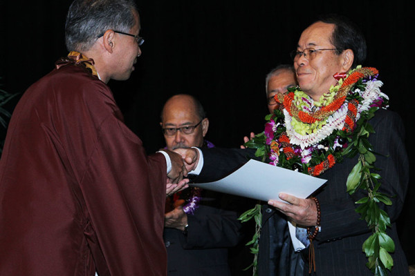 Bishop Matsumoto shakes hands with a smiling Rev. Tatsuo Muneto, who is wearing many lei