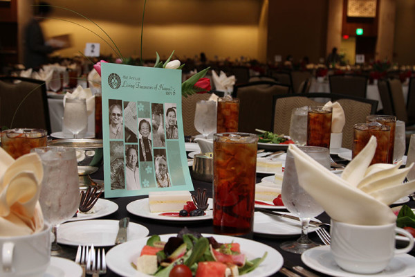Formal table setting with plates of food and iced tea and a Living Treasures Program in the center