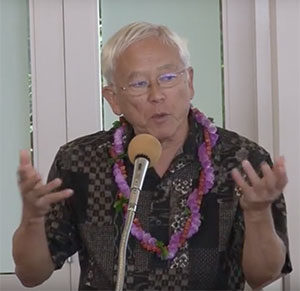 Dr. George Tanabe at the microphone, wearing lei and gesturing