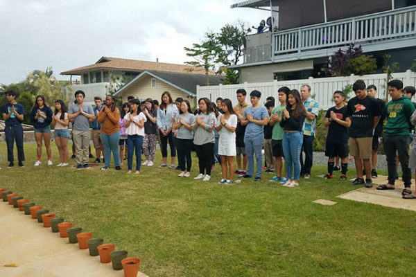 PBA students in gassho outside the PBA building before a bell and 17 pots for planting sunflowers, one for each victim.