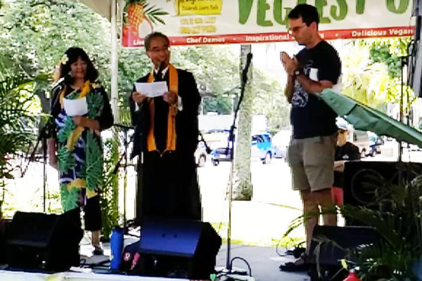 Bishop Matsumoto delivering aspiration/reflection at Peace Day at VegFest Oahu 2019, flanked by Wendie Yumori and David Atcheson