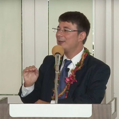 Duncan Williams wearing lei gestures at the podium