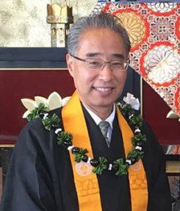 Bishop Eric Matsumoto at Annex Temple altar, wearing robes and kukui nut lei