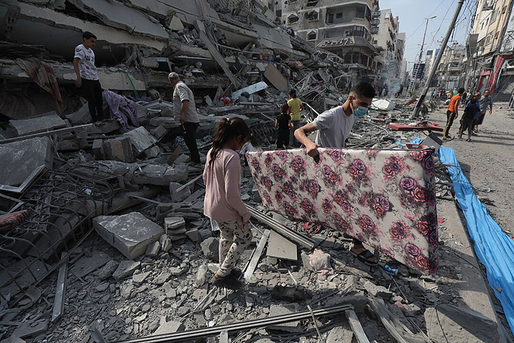 Children carrying mattress in bombed neighborhood in the Gaza Strip. By Palestinian News & Information Agency (Wafa) in contract with APAimages, CC BY-SA 3.0, https://commons.wikimedia.org/w/index.php?curid=138775595