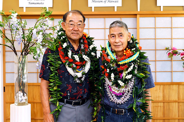Two smiling men side by side, each wearing many lei