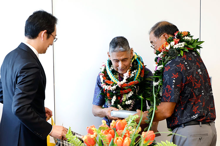 two men with lei holding a wrapped package while another man looks on