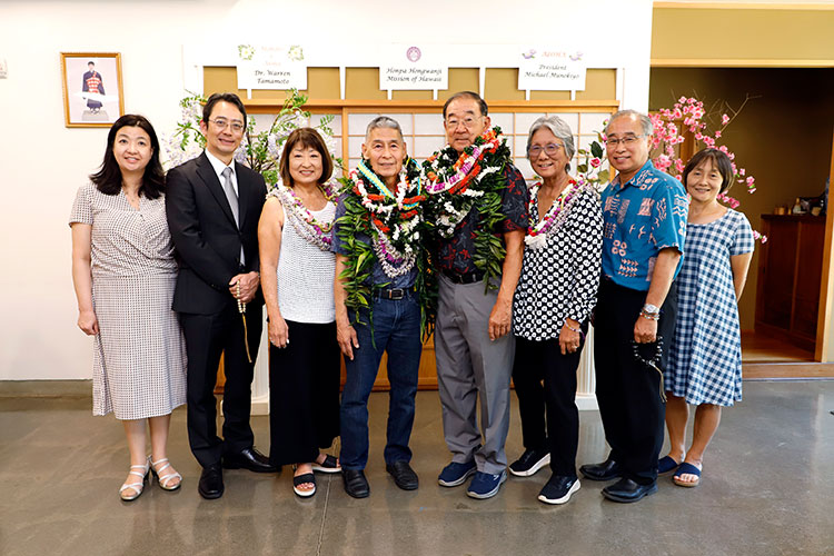 Eight people with two men wearing lei in the middle pose for a photo